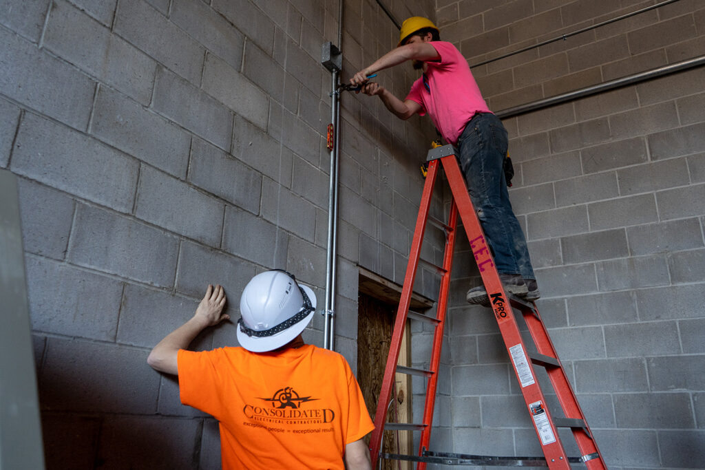 Consolidated Electrical Contractors workers installing electrical on ladder indoors