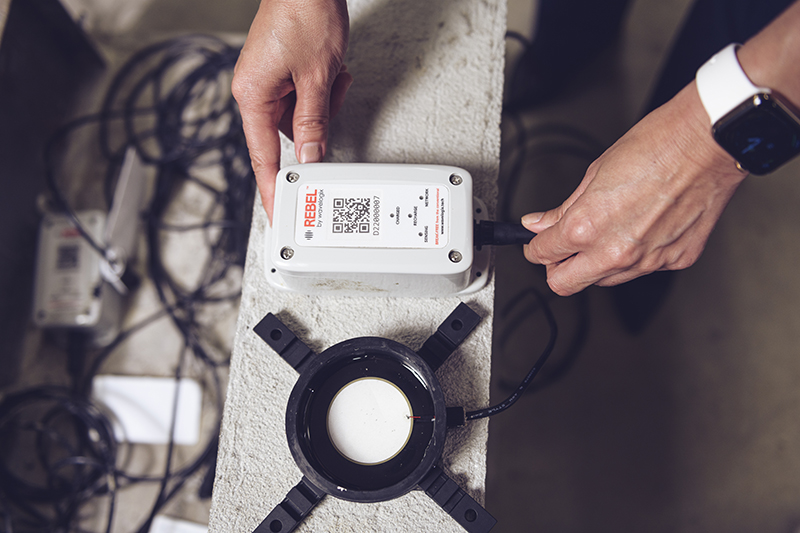 From beneath a concrete pour, this black circular sensor transmits data about the concrete’s strength levels through a cord plugged into an above-ground handheld device called a datalogger. Engineers receive real-time data from this device through a smartphone app. (Purdue University photo/Rebecca McElhoe)