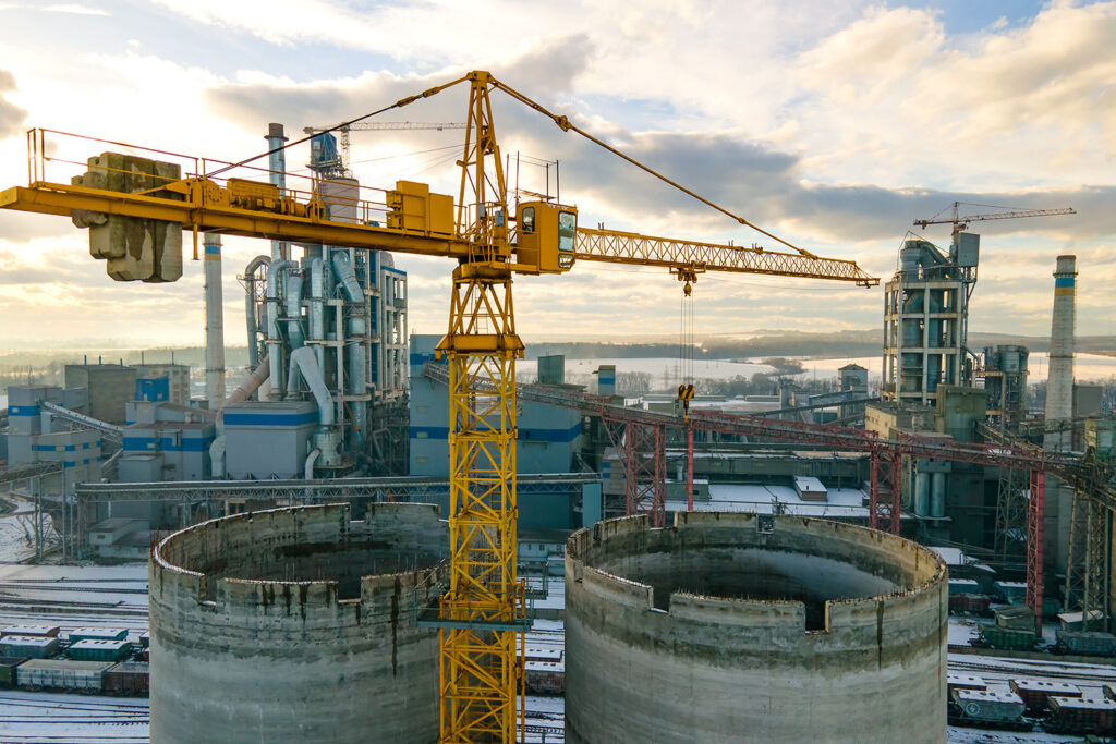 Aerial view of cement plant with high factory structure and tower crane at industrial production area.