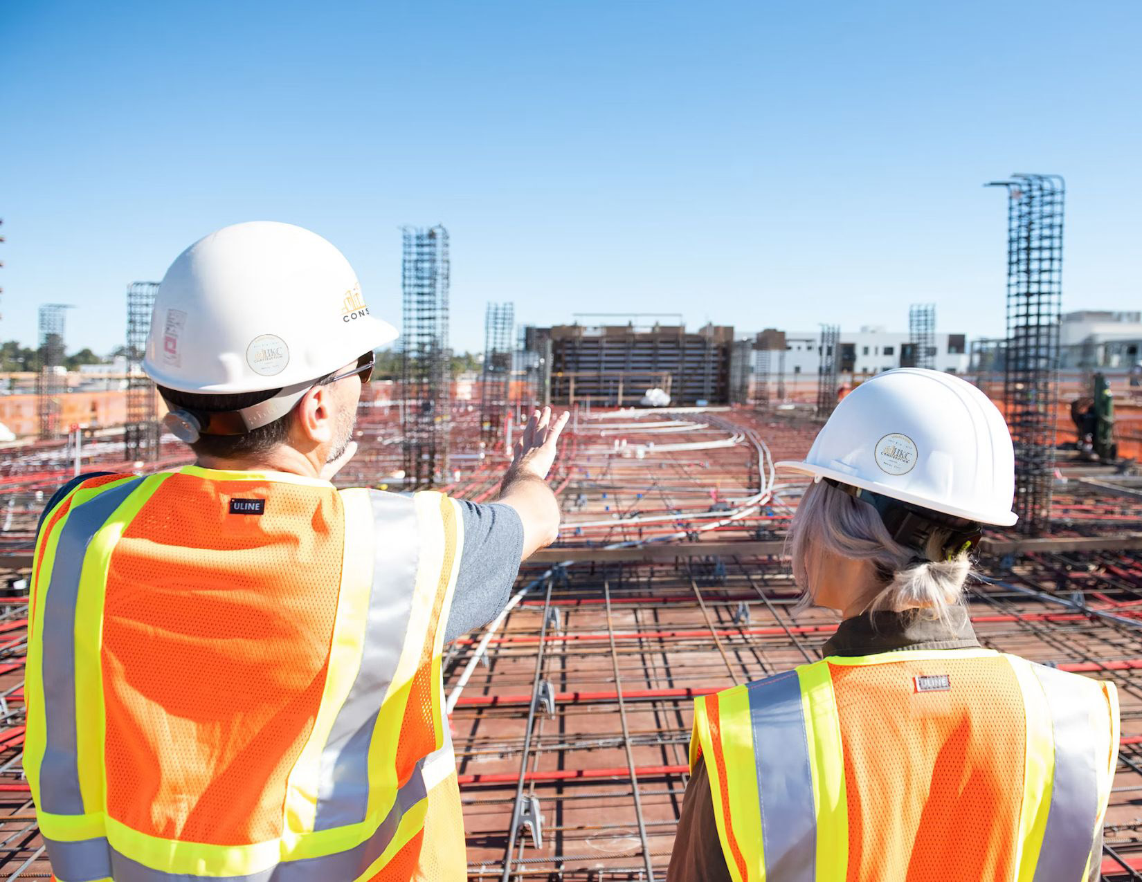 Two construction workers overlooking metal structure wearing safety gear.