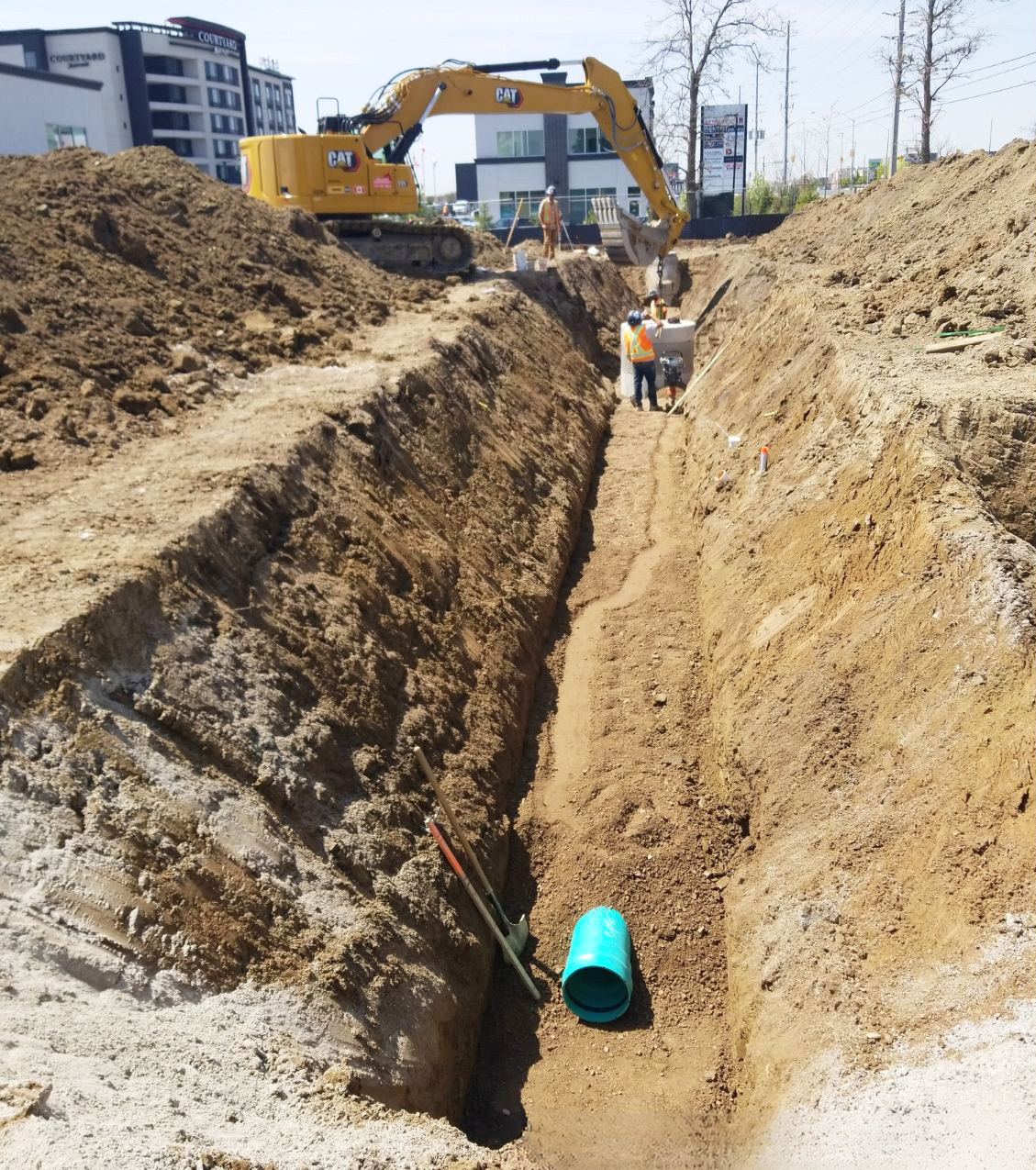 A construction site with a narrow hole dug in the ground for piping.