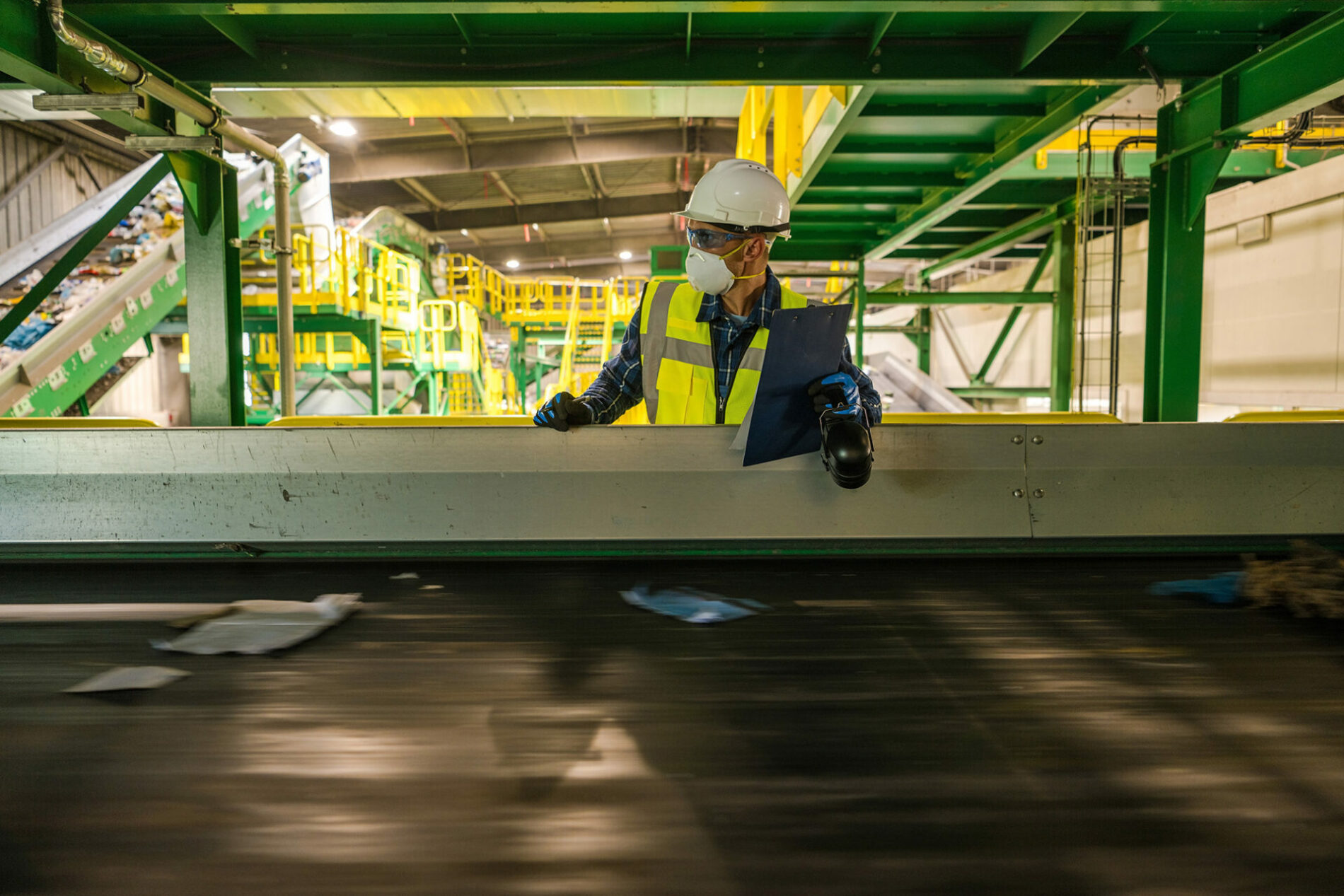 An image of man standing near conveyor belt in garbage facility.