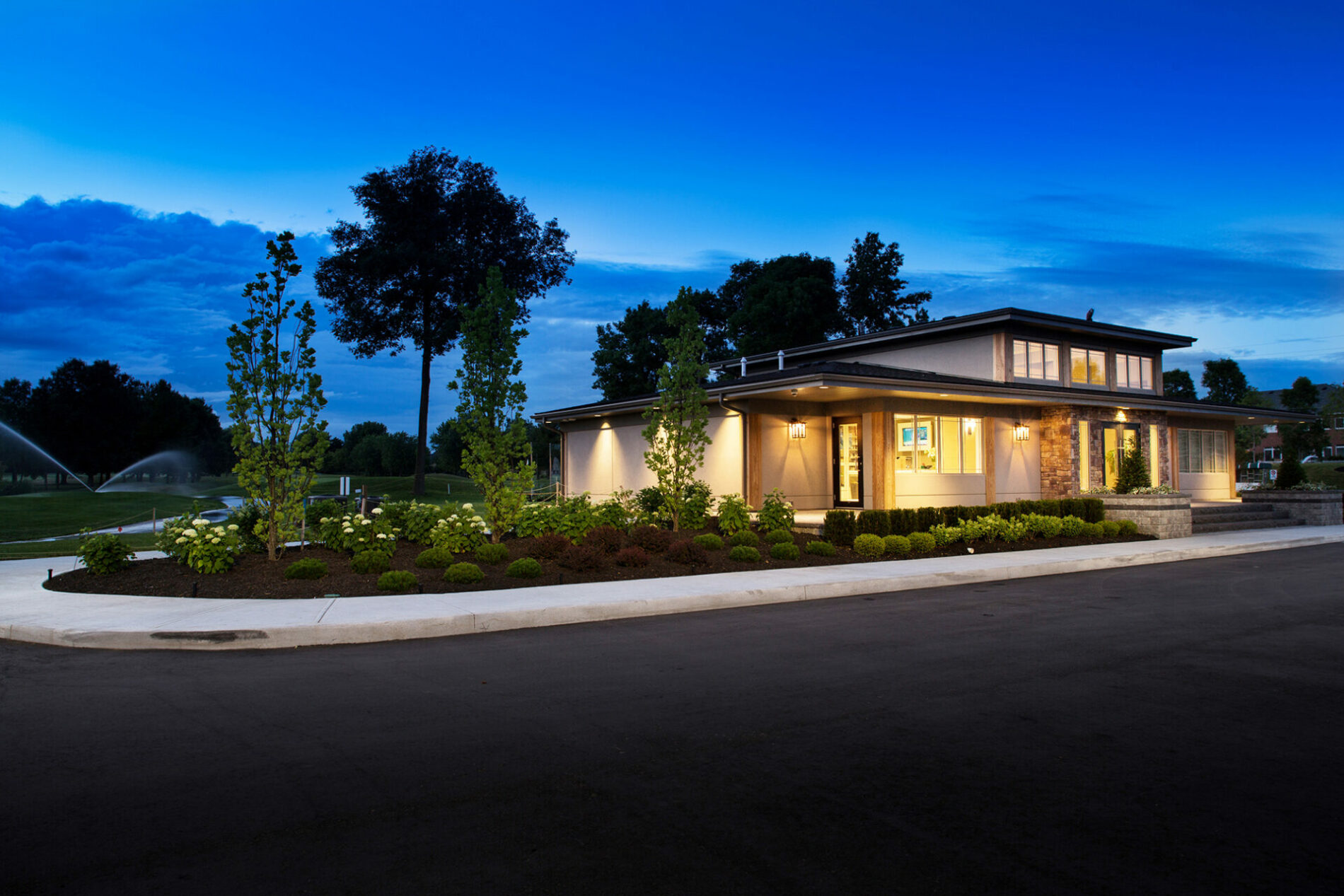 An image of a designed home at night with the lights on and dark blue skies.