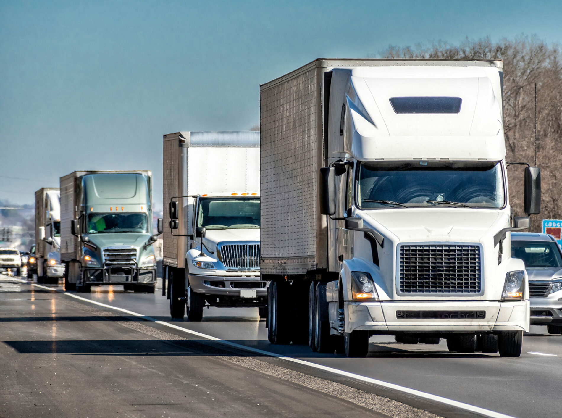 Horizontal shot of a convoy of eighteen wheeler turcks on an interstate highway.