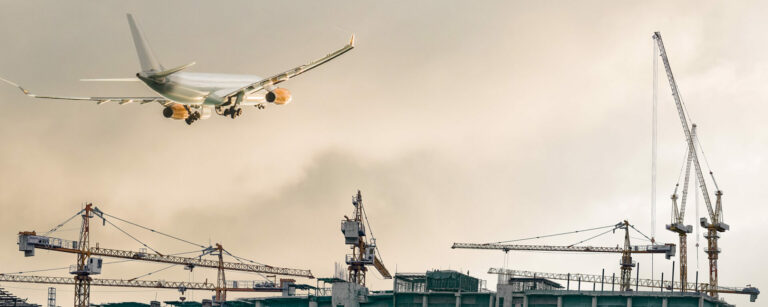 The airplane fly over the airport construction site with the tower crane operation and the background of cloudy sky